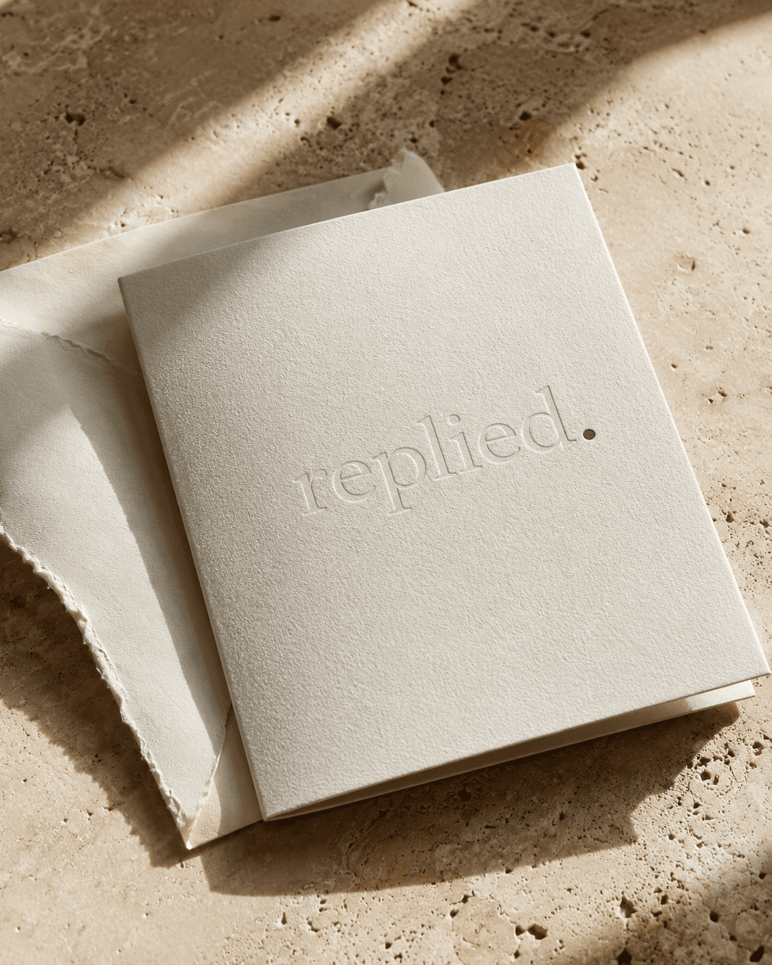An embossed replied. invitation resting on travertine stone